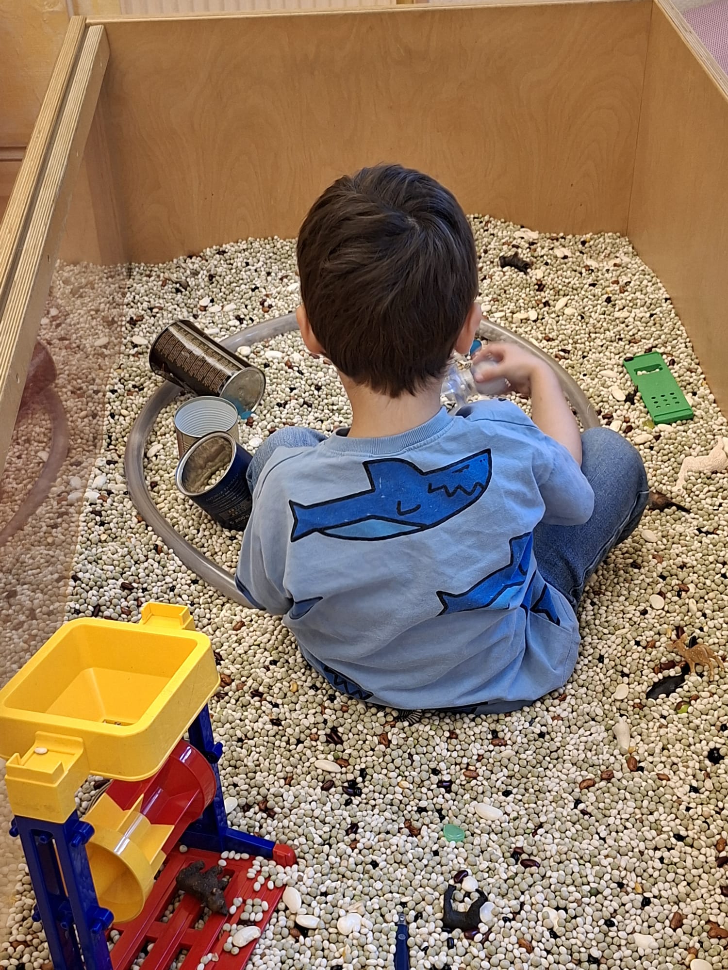 Kind sitzt in einem Bohnenbad und spielt mit kleinen Bechern und Figuren