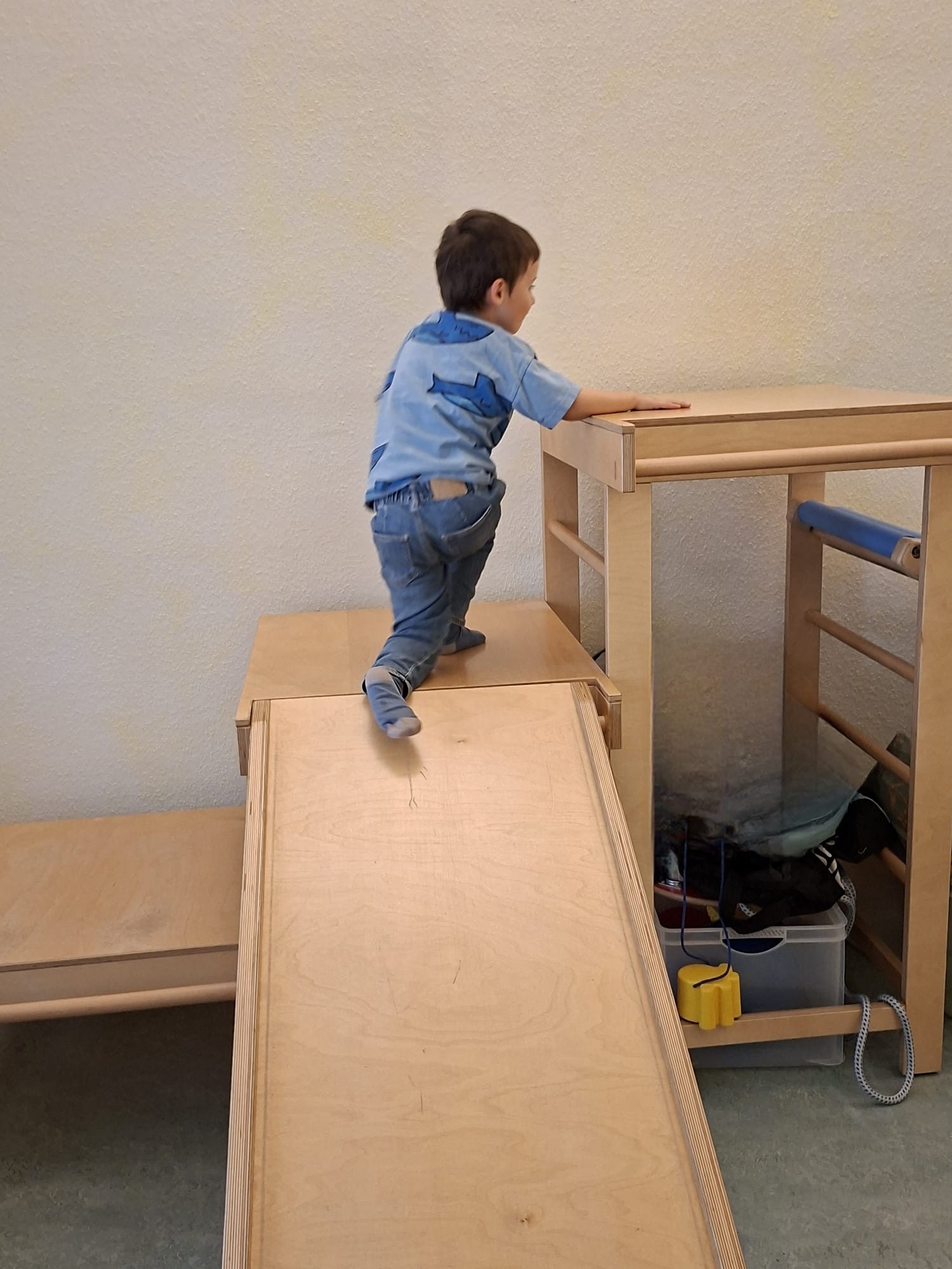 Kind klettert über ein Holzpodest mit schräger Rampe