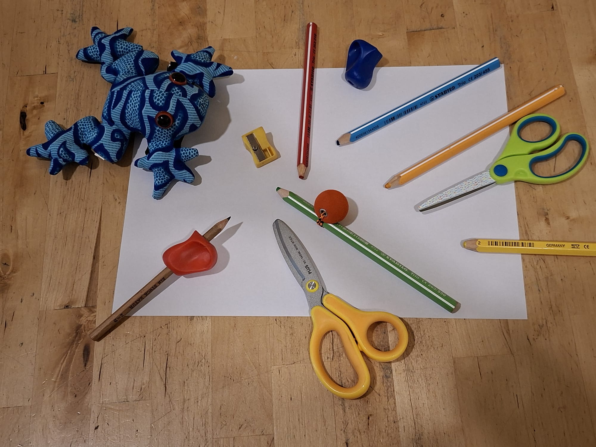 Therapiematerial für Kinder: Schere, Stifte, Stifthalter und Stoffkuscheltier auf einem Papier