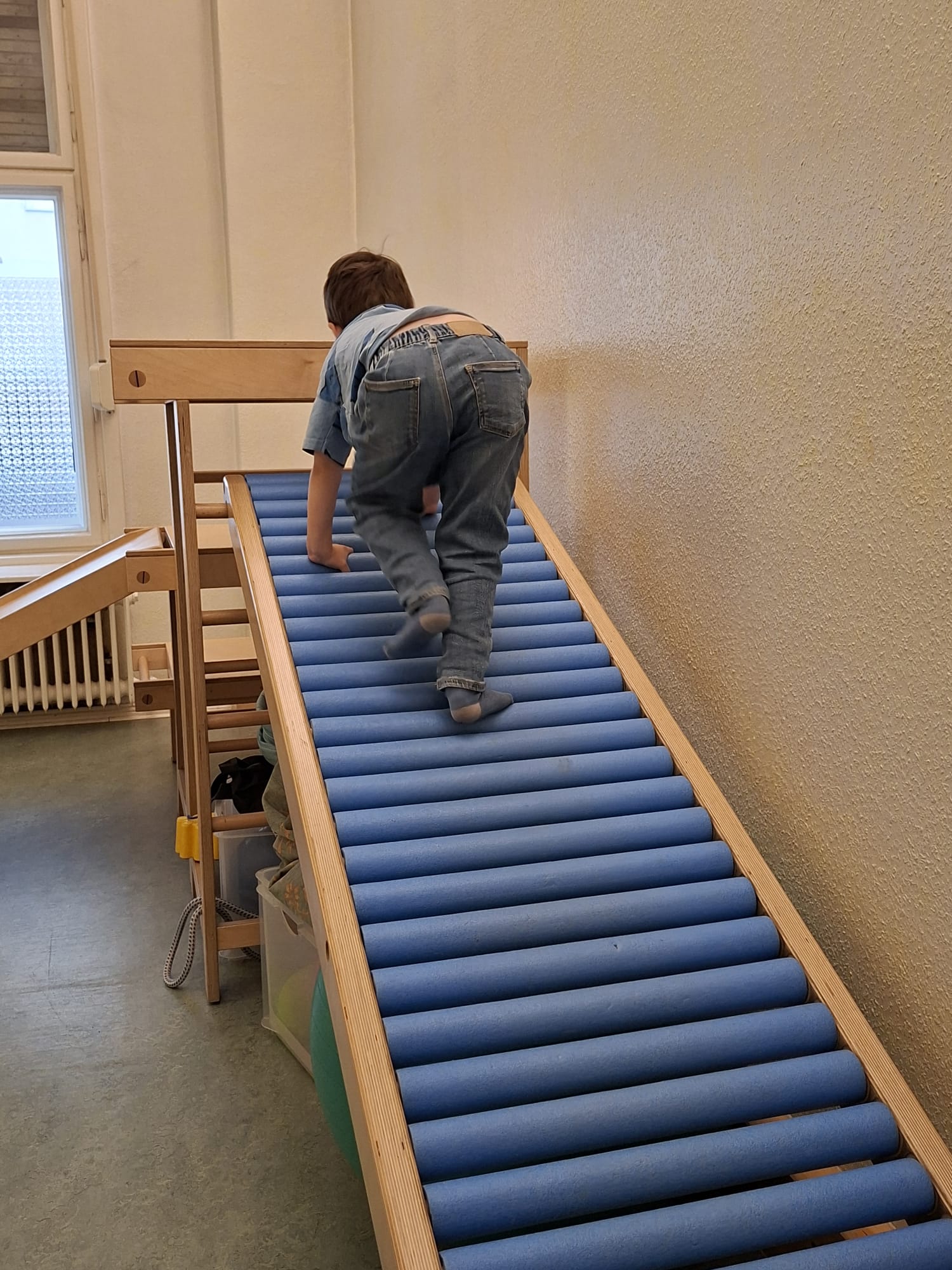 Kind klettert auf einer Rollenbahn mit blauen Rollen aus Holzrahmen