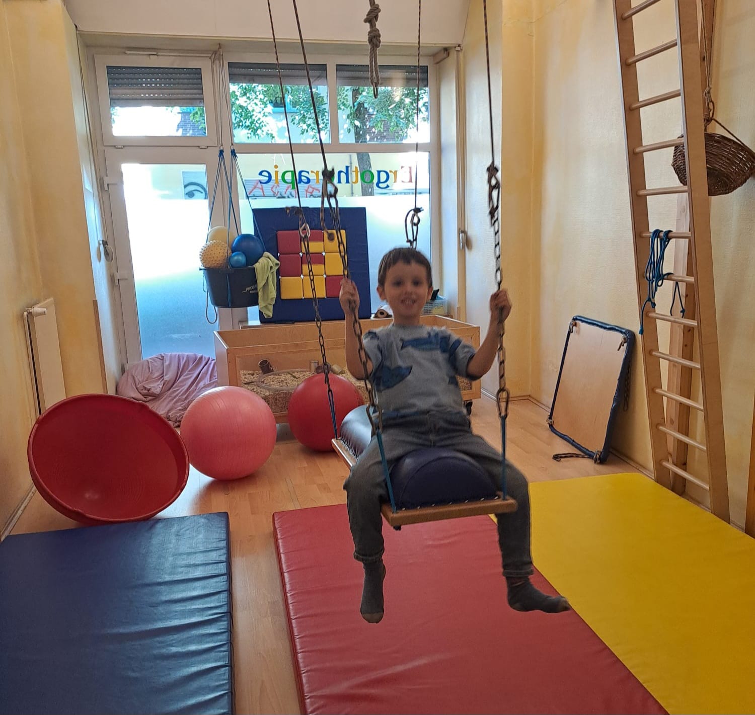 Kind sitzt lachend auf einer Therapieschaukel im Pädiatrieraum