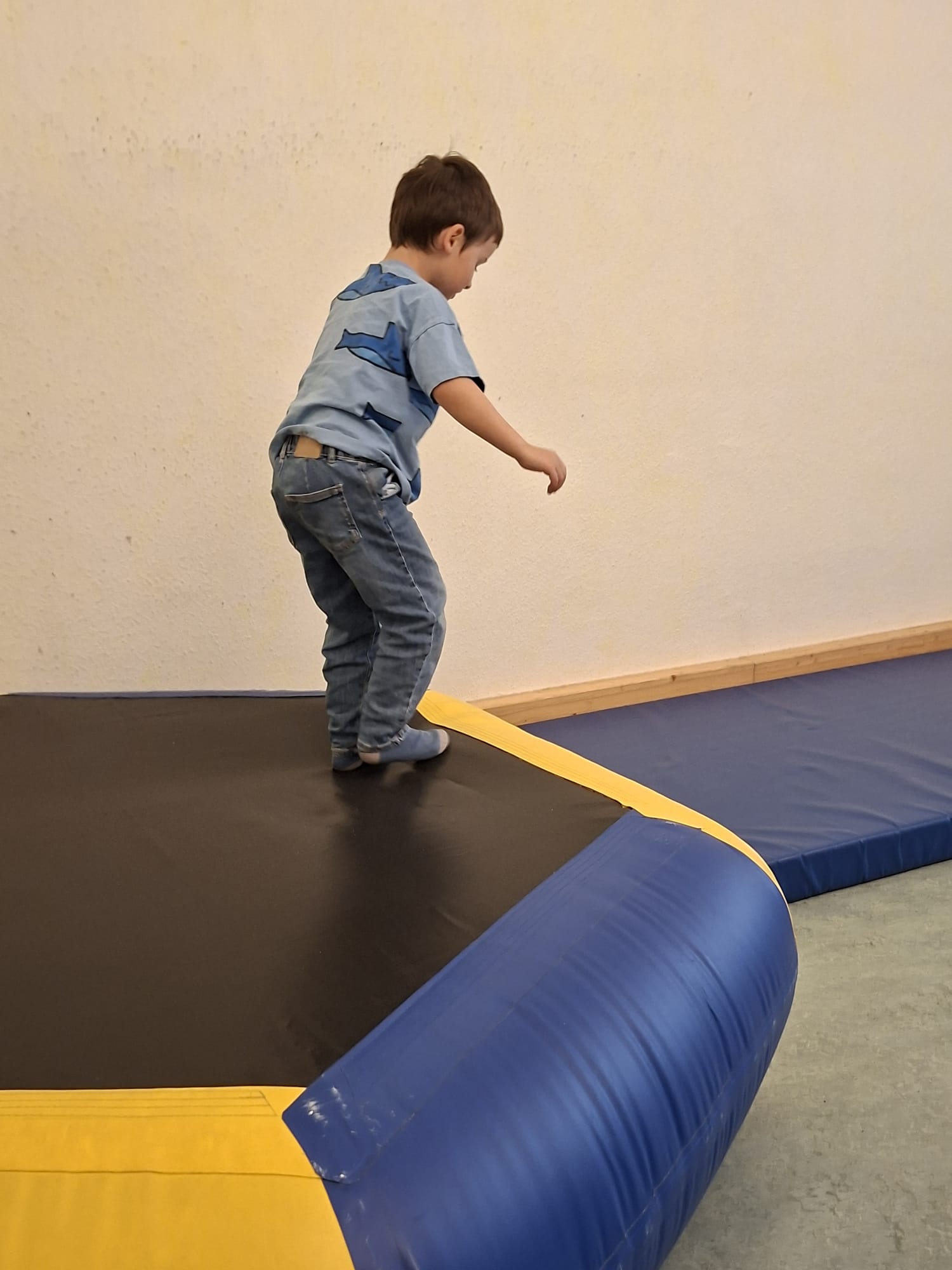 Kind springt auf einer großen Trampolinfläche mit blau-gelber Umrandung